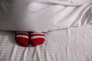 Photo of Woman wearing knitted socks under blanket in bed, closeup. Space for text