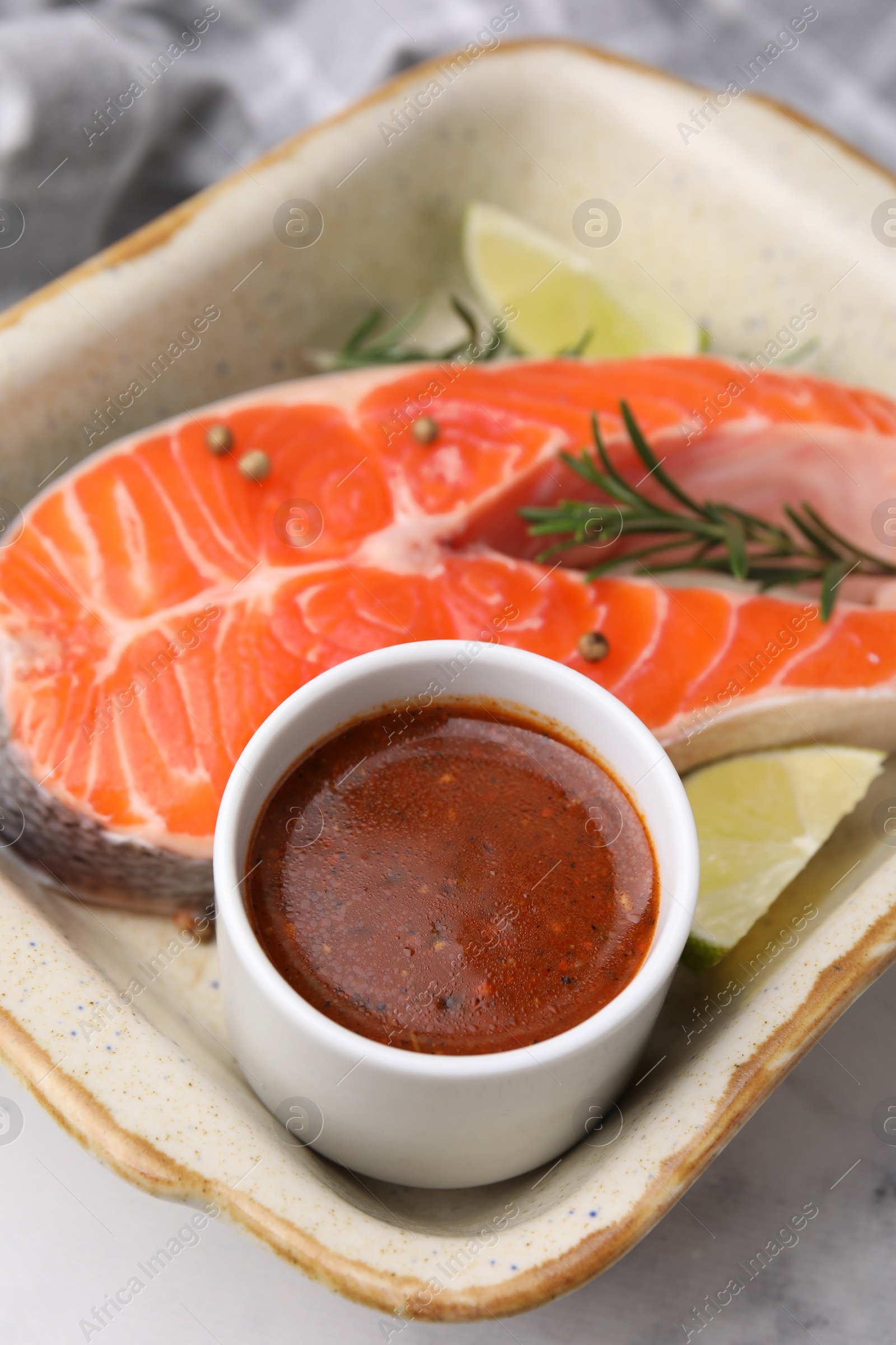 Photo of Fresh marinade, fish, lime and rosemary in baking dish on light table, closeup