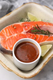 Fresh marinade, fish, lime and rosemary in baking dish on light table, closeup