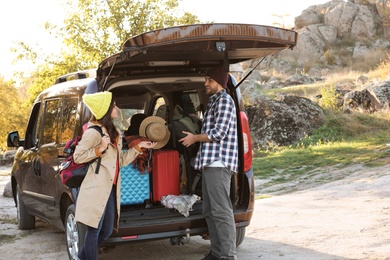 Young couple packing camping equipment into car trunk outdoors. Space for text