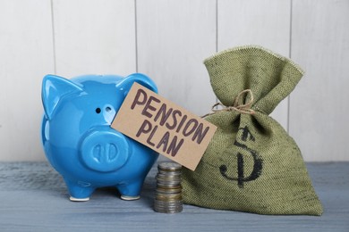 Photo of Card with phrase Pension Plan, stack of coins, sack and piggy bank on light blue wooden table. Retirement concept