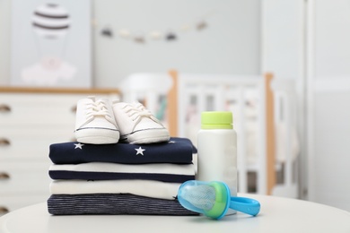 Stack of baby clothes, shoes and accessories on white table indoors