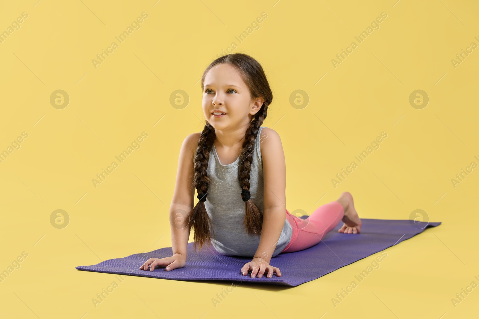 Photo of Cute little girl stretching on yellow background