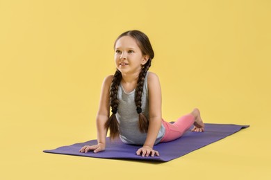 Cute little girl stretching on yellow background
