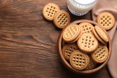 Photo of Tasty sandwich cookies with cream and glass of milk on wooden table, flat lay. Space for text