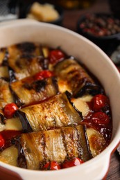 Tasty eggplant rolls with tomatoes and cheese in baking dish on table, closeup