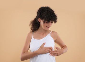 Photo of Beautiful young woman doing breast self-examination on light brown background