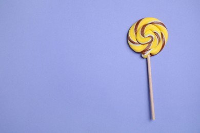 Stick with colorful lollipop swirl on violet background, top view. Space for text