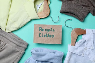 Photo of Recycling concept. Clothes and card with phrase on turquoise background, flat lay