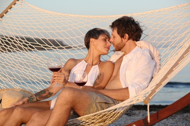 Photo of Young couple resting with glasses of wine in hammock on beach