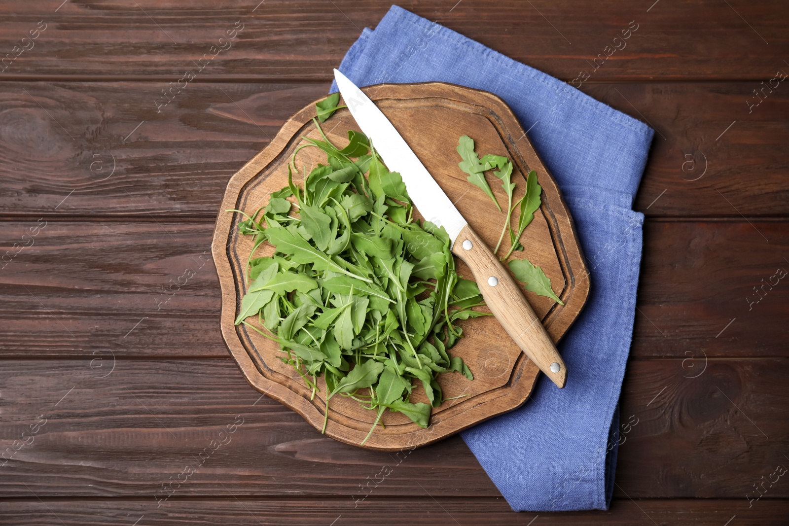 Photo of Cutting board with fresh arugula leaves and knife on wooden table, flat lay