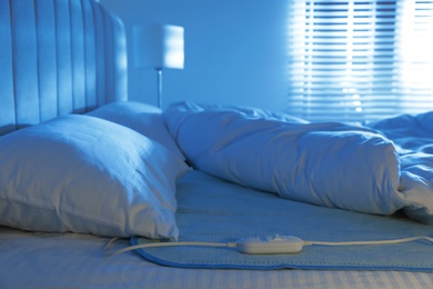 Photo of Bed with electric heating pad indoors at night