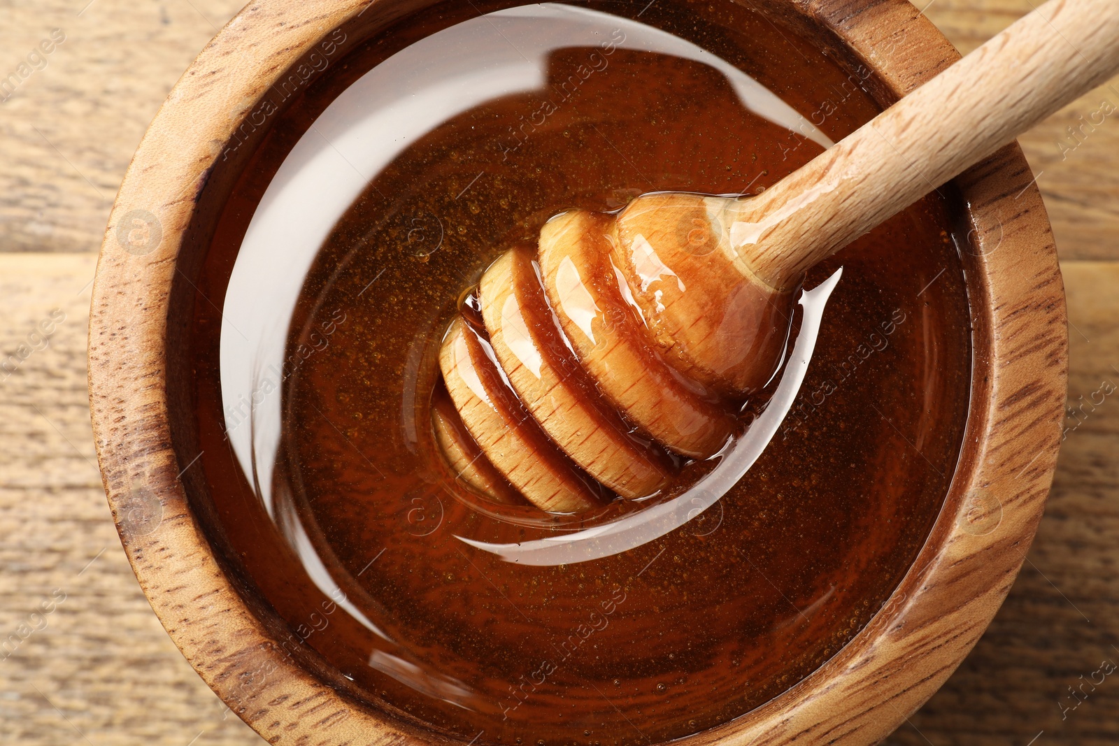 Photo of Dipper with honey in bowl on wooden table, top view