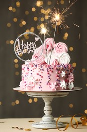 Photo of Beautiful birthday cake with festive decor and sparkles on white table