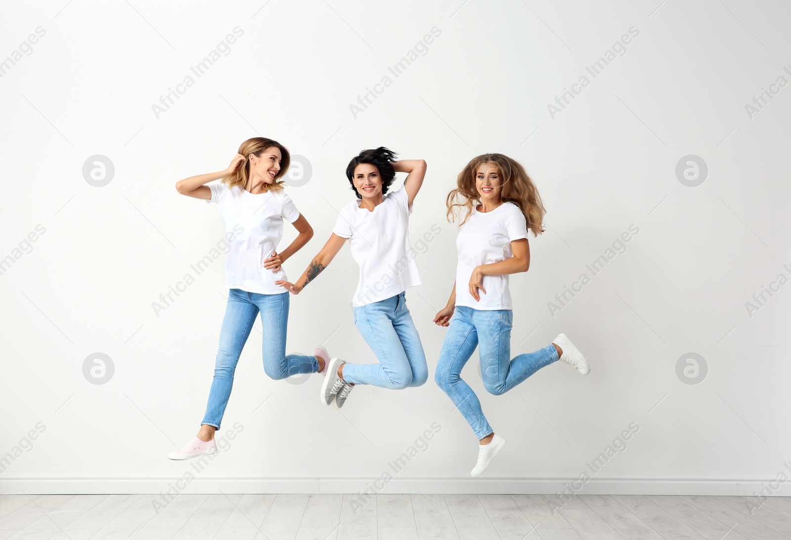 Photo of Group of young women in jeans jumping near light wall