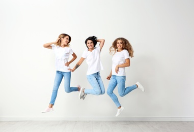 Group of young women in jeans jumping near light wall