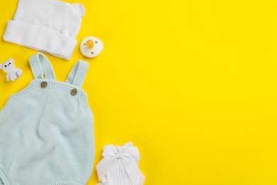 Flat lay composition with baby clothes and accessories on yellow background, space for text