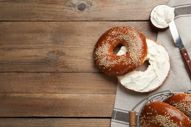 Photo of Delicious bagel with cream cheese on wooden table, flat lay. Space for text