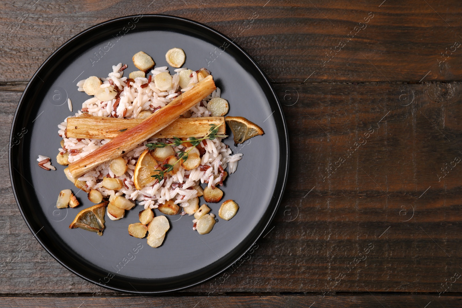 Photo of Plate with baked salsify roots, lemon and rice on wooden table, top view. Space for text