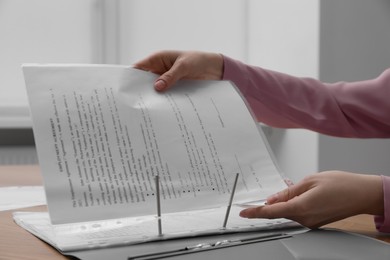 Woman putting punched pocket with document into folder at table, closeup