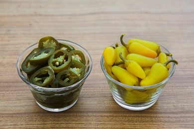 Glass bowls of pickled green and yellow jalapeno peppers on wooden table