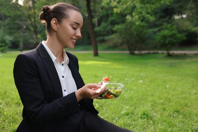 Lunch time. Happy businesswoman with container of salad on green grass in park, space for text