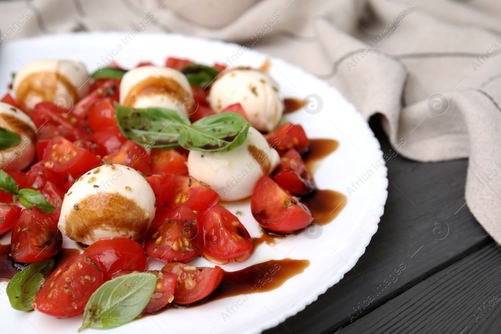 Photo of Tasty salad Caprese with tomatoes, mozzarella balls, basil and balsamic vinegar on grey wooden table, closeup