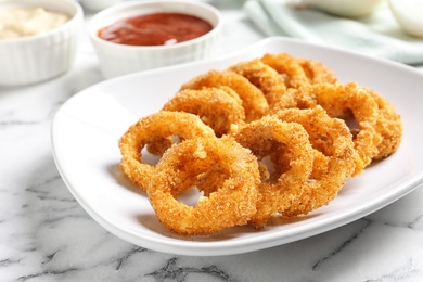 Photo of Plate with homemade crunchy fried onion rings and sauce on marble table, closeup