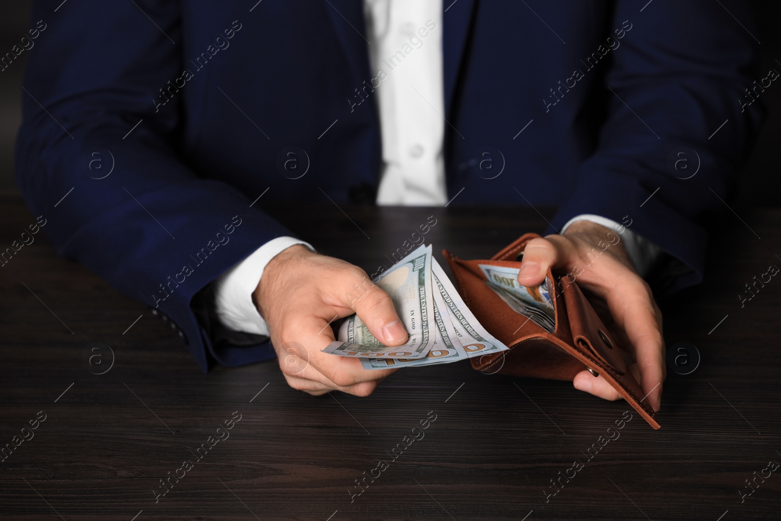 Photo of Businessman holding wallet with dollar bills at wooden table, closeup