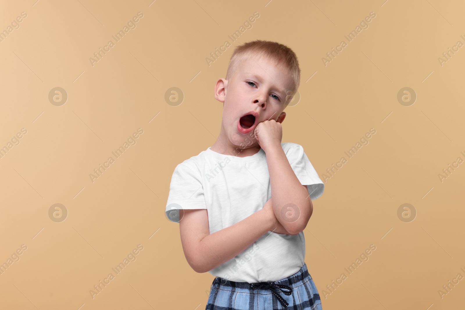 Photo of Sleepy boy yawning on beige background. Insomnia problem