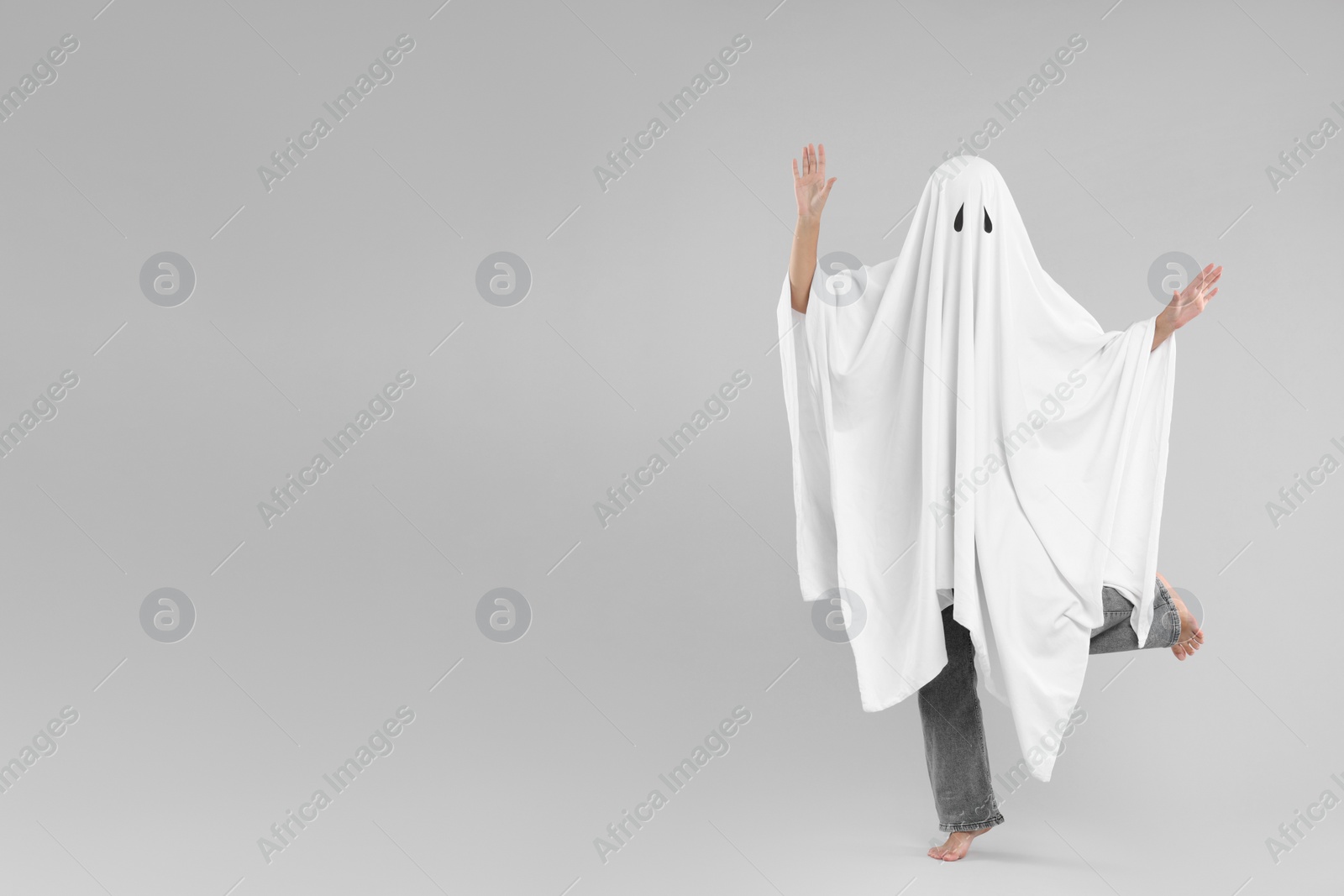 Photo of Woman in white ghost costume on light grey background, space for text. Halloween celebration