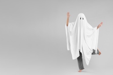Woman in white ghost costume on light grey background, space for text. Halloween celebration