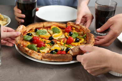 Women taking slices of delicious vegetable pizza at grey table, closeup