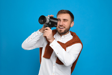 Photo of Young man with vintage video camera on light blue background