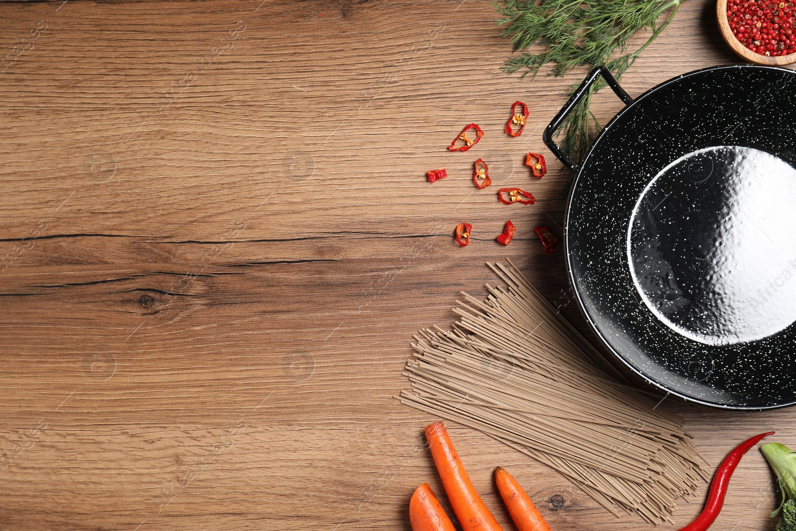 Photo of Empty iron wok surrounded by raw ingredients on wooden table, flat lay. Space for text