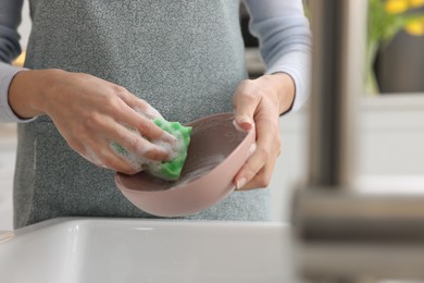 Woman washing plate above sink in modern kitchen, closeup