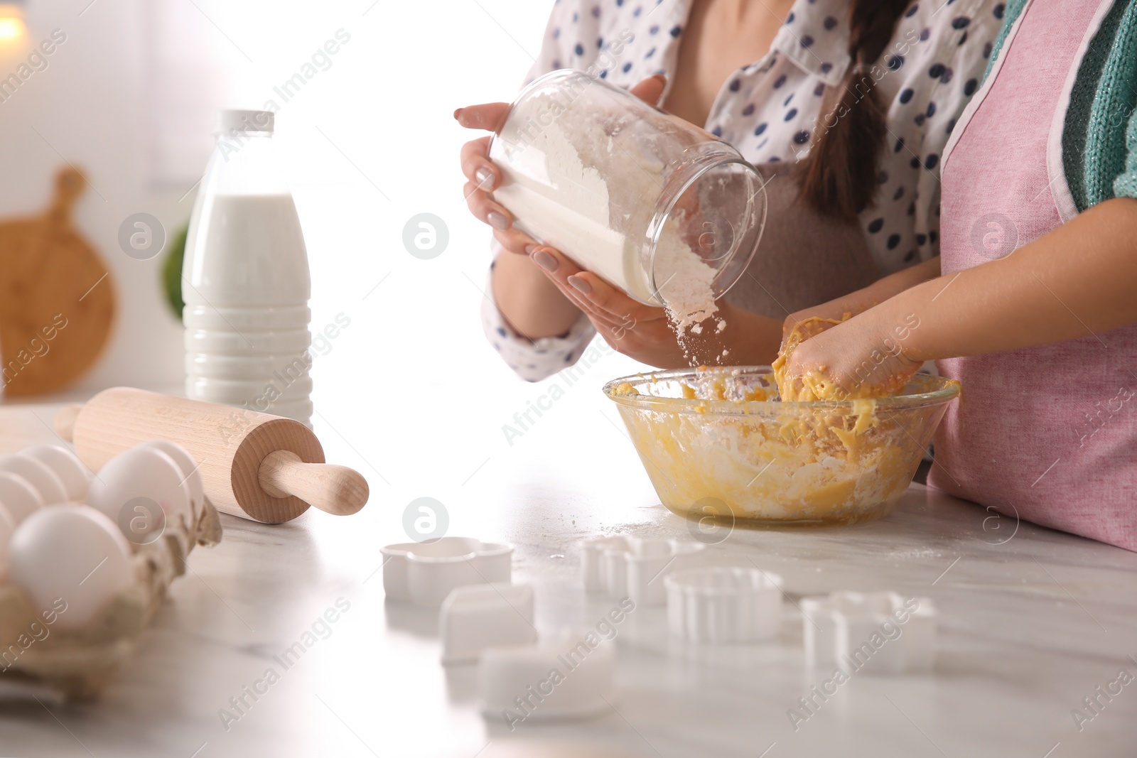 Photo of Mother and daughter making dough at table in kitchen, closeup