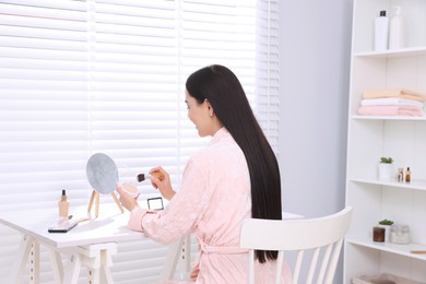 Photo of Young woman with powder and brush at dressing table indoors