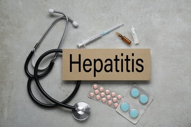 Photo of Cardboard with word Hepatitis and medical supplies on light grey table, flat lay