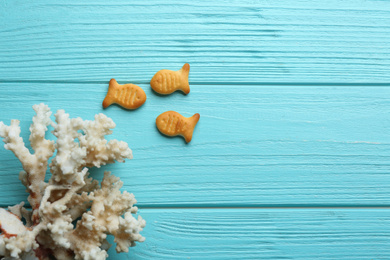 Photo of Delicious goldfish crackers and coral on light blue wooden table, flat lay. Space for text