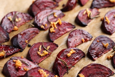 Photo of Roasted beetroot slices with garlic and rosemary on parchment, closeup