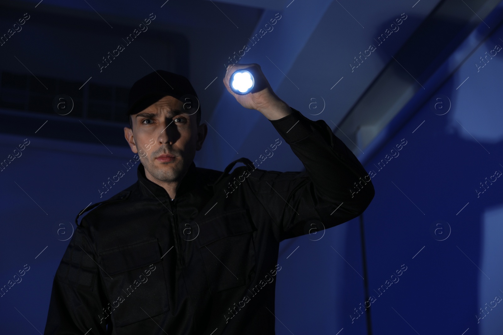 Photo of Male security guard with flashlight in dark room