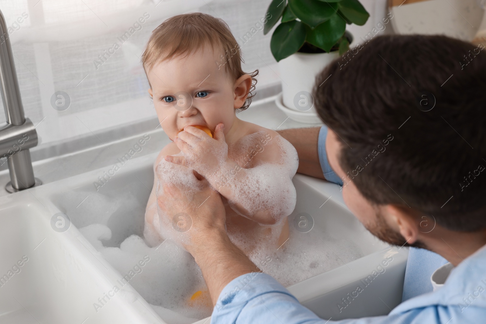 Photo of Father washing his little baby in sink indoors