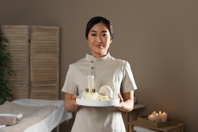 Photo of Portrait of young Asian masseur holding tray with spa stuff in salon