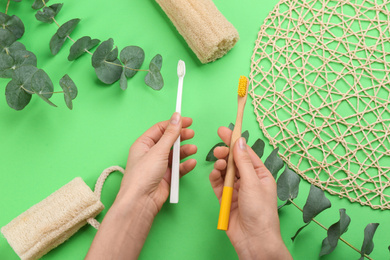 Photo of Woman holding natural bamboo and plastic toothbrushes over green background, top view