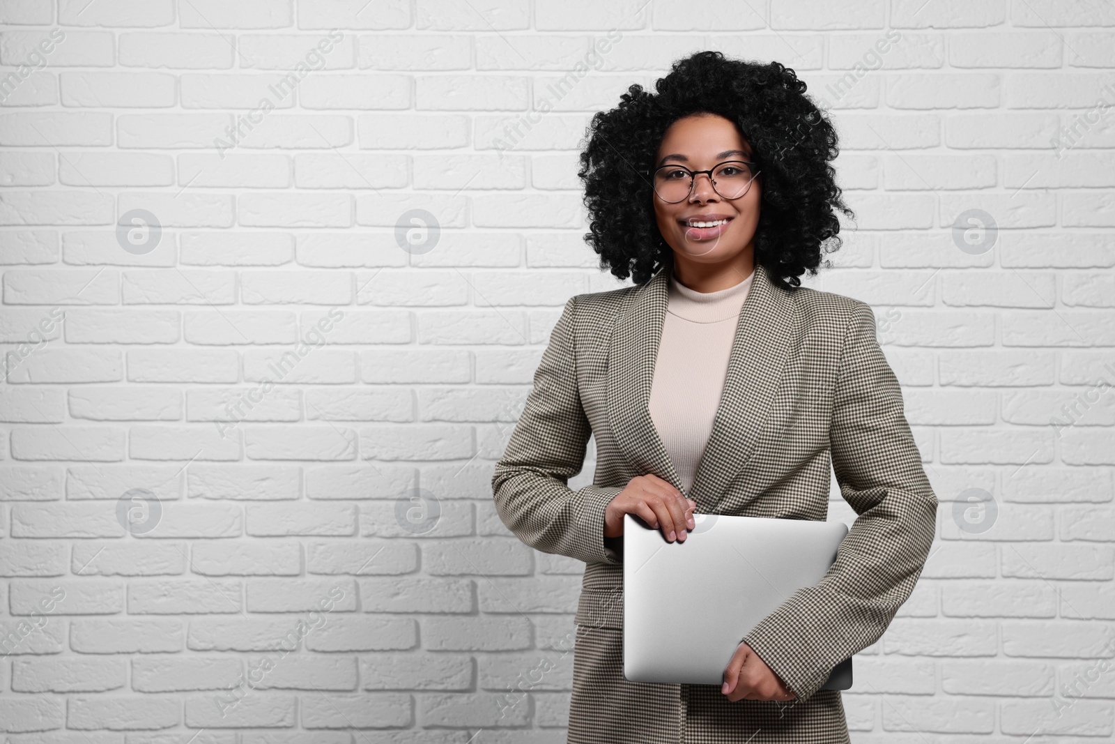 Photo of Young businesswoman holding laptop near white brick wall. Space for text