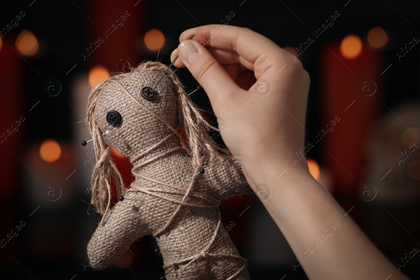 Photo of Woman stabbing voodoo doll with pin in dark room, closeup. Curse ceremony