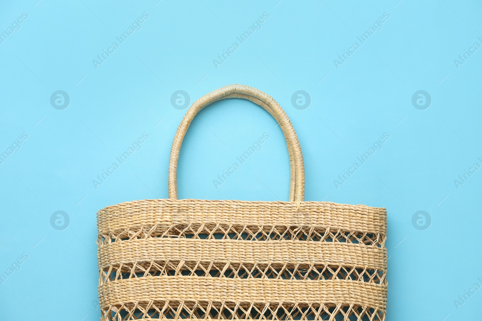 Photo of Elegant woman's straw bag on light blue background, top view