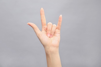 Woman showing hand sign on grey background, closeup. Body language