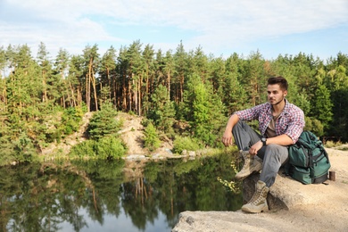 Young man on rock near lake and forest. Camping season